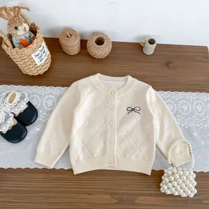 Gestrickte beige Baby-Strickjacke mit Rautenmuster und Bogenstickerei auf Holzgrund