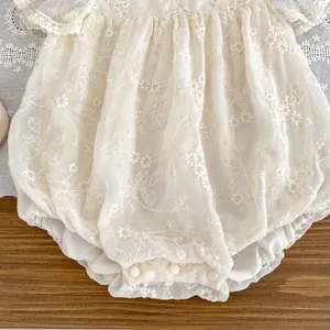 Detail of baby romper featuring floral embroidery, lace trims, and bottom snap buttons