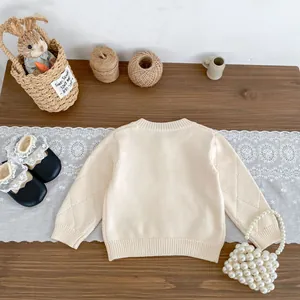 Details der cremefarbenen Baby-Strickjacke mit Rautenmuster und gerippten Bündchen