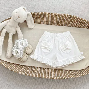 Detail of white cotton baby shorts with heart-shaped bow pockets and lace-up shoes