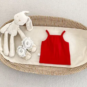 Detail of red ribbed cotton baby tank top with baby shoes in a woven basket