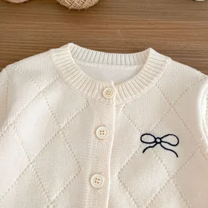 Detailaufnahme der cremefarbenen Strickjacke mit Rautenmuster und schwarzer Schleife