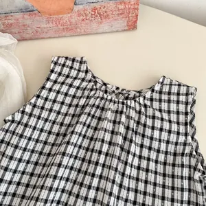 Detail of toddler sleeveless top featuring black and white plaid pattern and pleated neckline