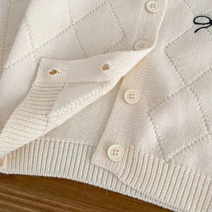Detail der cremefarbenen Strickjacke mit Rautenmuster und schwarzer Buchstabenstickerei