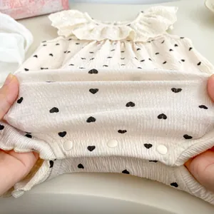 Détail de barboteuse bébé avec col en dentelle, motifs cœurs et boutons-pression bas