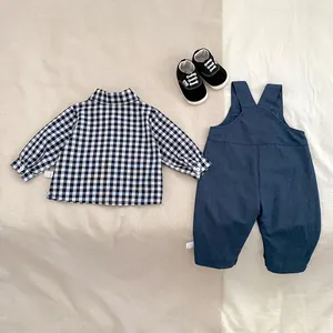Flat lay of baby boy plaid shirt and navy overalls set with small black canvas shoes