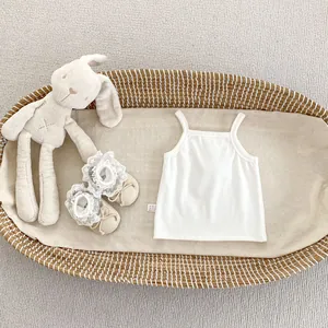 Flat lay of white ribbed baby tank top with lace shoes and bunny in a wicker basket
