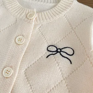 Details der cremefarbenen Strickjacke mit Rautenmuster und schwarzer Schleifenstickerei