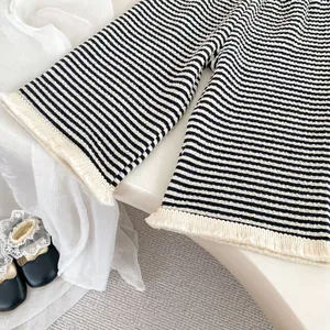 Dettaglio di pantaloni in maglia a righe per neonata con nappe beige decorative sull'orlo