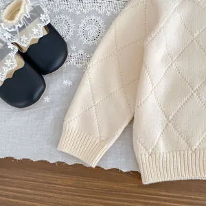 Detailaufnahme von cremefarbenem Baby-Strickpullover mit Rautenmuster und Spitzenschuhen