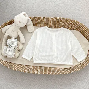 Detailansicht der weißen gerippten Baby-Strickjacke in einem geflochtenen Babykorb