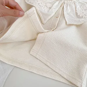 Nahaufnahme der beigen Waffelstrickjacke mit floralem Spitzenkragen und feiner Naht