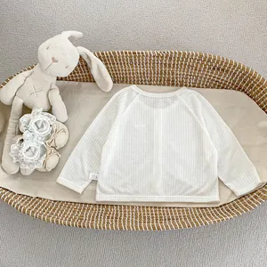 Détail du cardigan blanc côtelé pour bébé dans un panier tressé avec des jouets