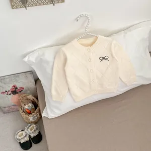 Details einer cremefarbenen Strickjacke mit Rautenmuster und kleiner schwarzer Schleife