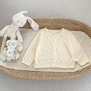Détail d'un cardigan en maille crème pour bébé avec nœud jaune dans un panier tressé