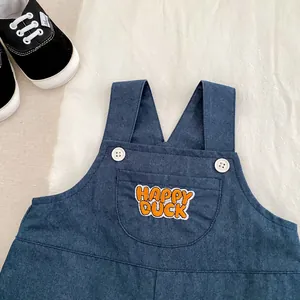 Detail of dark blue denim baby overalls with Happy Duck embroidery and white buttons