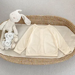 Vue détaillée d'un gilet bébé beige à mailles côtelées sur un panier en osier