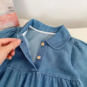 Detail view of the Peter Pan collar and wooden buttons on this light blue denim baby romper