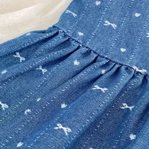 Detail of blue denim fabric with white embroidered bows and delicate pleated stitching