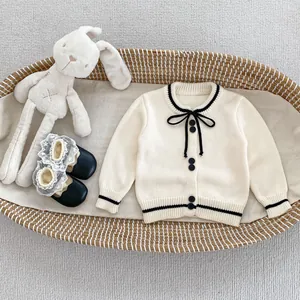Close-up of cream knit cardigan with black bow detail and lace-trimmed shoes in a basket