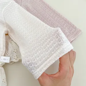Dettaglio macro della maglia pointelle e bordo in pizzo bianco sul cardigan neonato