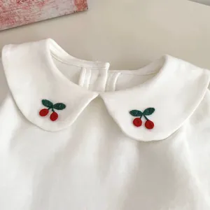Dettaglio del top in cotone bianco con colletto Peter Pan e ricamo a ciliegia rossa