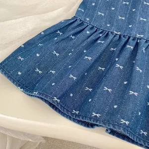 Detail of blue denim dress with white bow embroidery and ruffled hemline texture