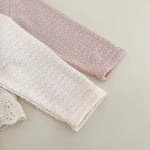 Dettaglio della manica di cardigan per neonati con trama a nido d'ape e pizzo ricamato