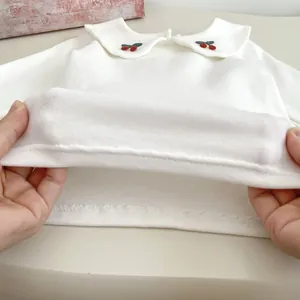 Dettaglio della maglia bianca in cotone per neonati con ricamo a ciliegia e tessuto