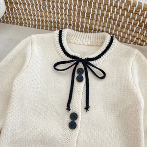 Detailed close-up of cream knit cardigan featuring black trim and bow tie detail