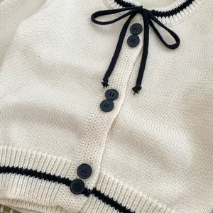 Detailed macro view of cream knit cardigan featuring black bow tie and contrast trim