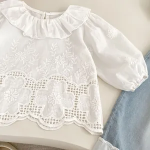 Close-up of white girls' blouse featuring eyelet lace hem and floral embroidery