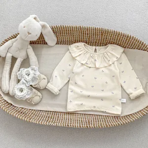 Close-up of beige baby top with blue bow print and elegant lace collar in a basket