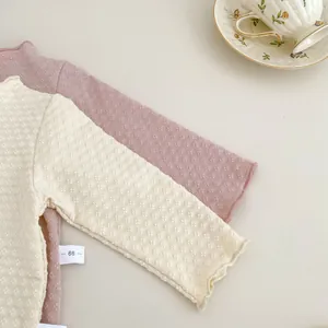 Nahaufnahme von Baby-Oberteilen aus Jacquard-Strick mit verspielten Wellenkanten-Details