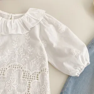 Detail of girls white cotton shirt featuring floral embroidery and ruffled collar lace
