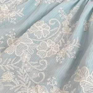 Nahaufnahme des hellblauen Babykleid-Stoffs mit feiner weißer Blumenstickerei im Detail