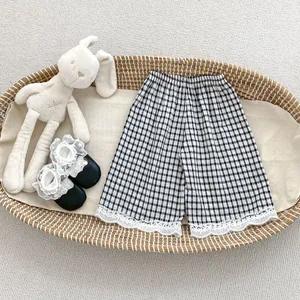 Detailed view of kids checkered wide-leg pants with delicate white lace trim on the hem