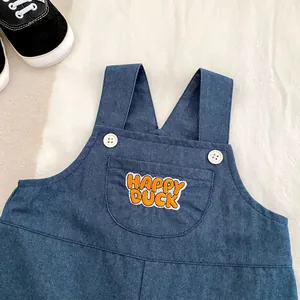 Detail of dark blue denim overalls featuring an orange Happy Duck embroidered pocket