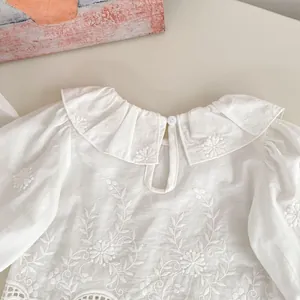 Detailed view of white cotton girls shirt with flower embroidery and ruffled collar