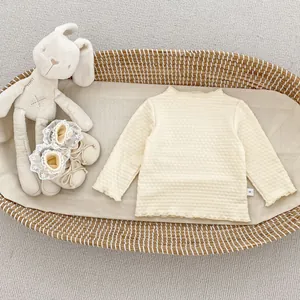 Detail eines beigen Baby-Strickoberteils mit Rüschenrand und Etikett im Korb