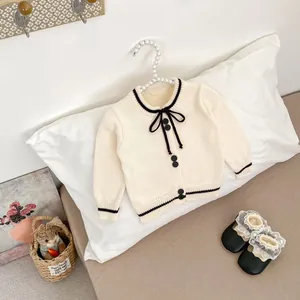 Detailed close-up of cream knit cardigan with black contrast trim and bow decoration