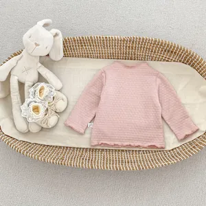 Detail eines rosa Baby-Oberteils mit Waffelstruktur, Rüschen und Plüsch-Hasen-Spielzeug