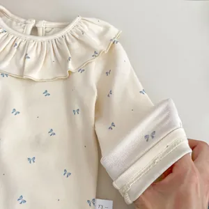 Detailed view of baby shirt featuring blue bow prints, ruffle collar and size label