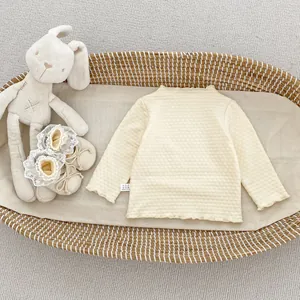 Detailaufnahme des cremefarbenen Baby-Strickoberteils mit Wellensaum im Weidenkorb