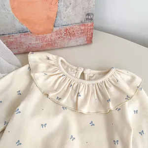 Detail view of baby beige top featuring ruffle lace collar and blue bow patterns