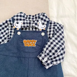 Detail of baby boy gingham shirt with duck patch and denim overalls with orange embroidery