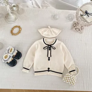 Detail view of girls knitted cardigan with black contrast trim and bow on white fabric