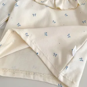 Detail of cream baby top featuring small blue bow prints and delicate ruffle collar