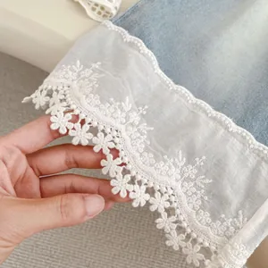 Detailed close-up of white floral lace embroidery on light blue denim jeans hemline