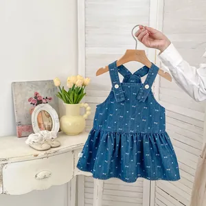 Detail of dark blue denim pinafore dress with white bow prints and ruffled hem